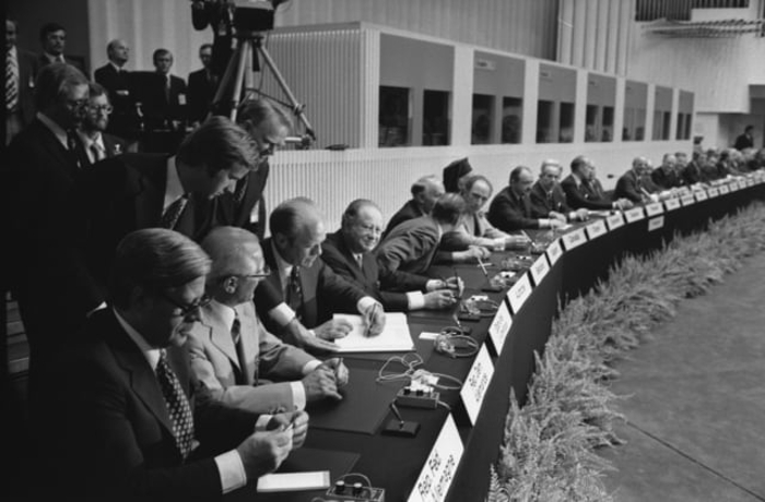 Photograph of President Gerald R. Ford Signing the Final Act of the Conference on Security and Cooperation in Europe as It Is Passed Among European Leaders for Signature in Finlandia Hall in Helsinki, Finland