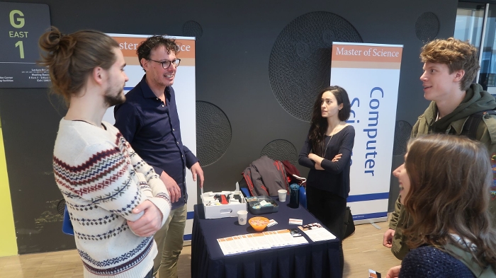 Docent Maarten Lamers praat met twee van zijn studenten en twee bezoekers. Op de tafel ligt de drone voor zijn presentatie al klaar.