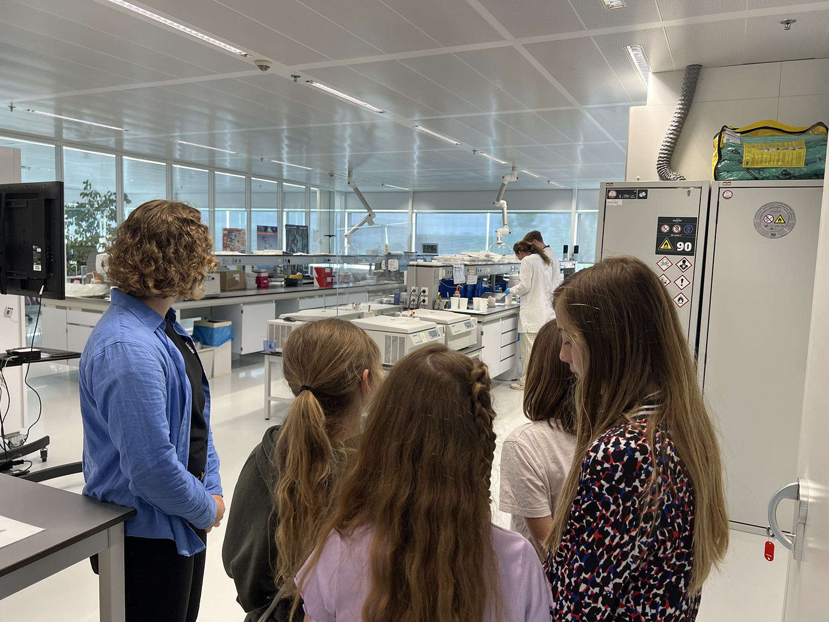 Children are shown around a laboratory room, with laboratory equipment in the background.