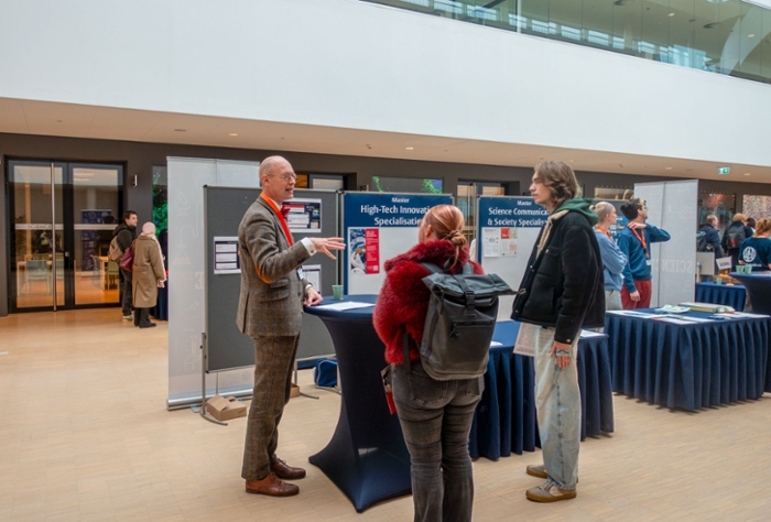 A man in a suit stands at a table and talks to a female and a male student.
