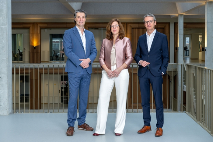 Three board members, a woman flanked by two men, pose in a modern office environment.