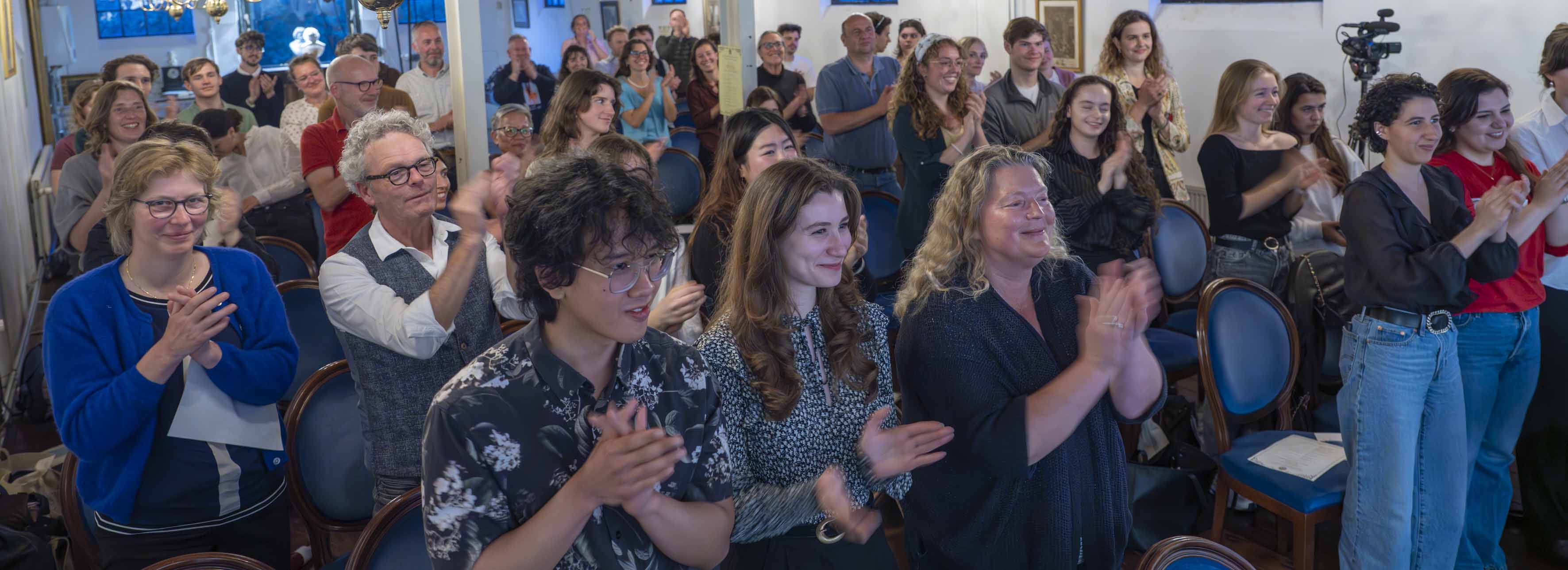 Staande ovatie van het publiek, glimlachende gezichten.