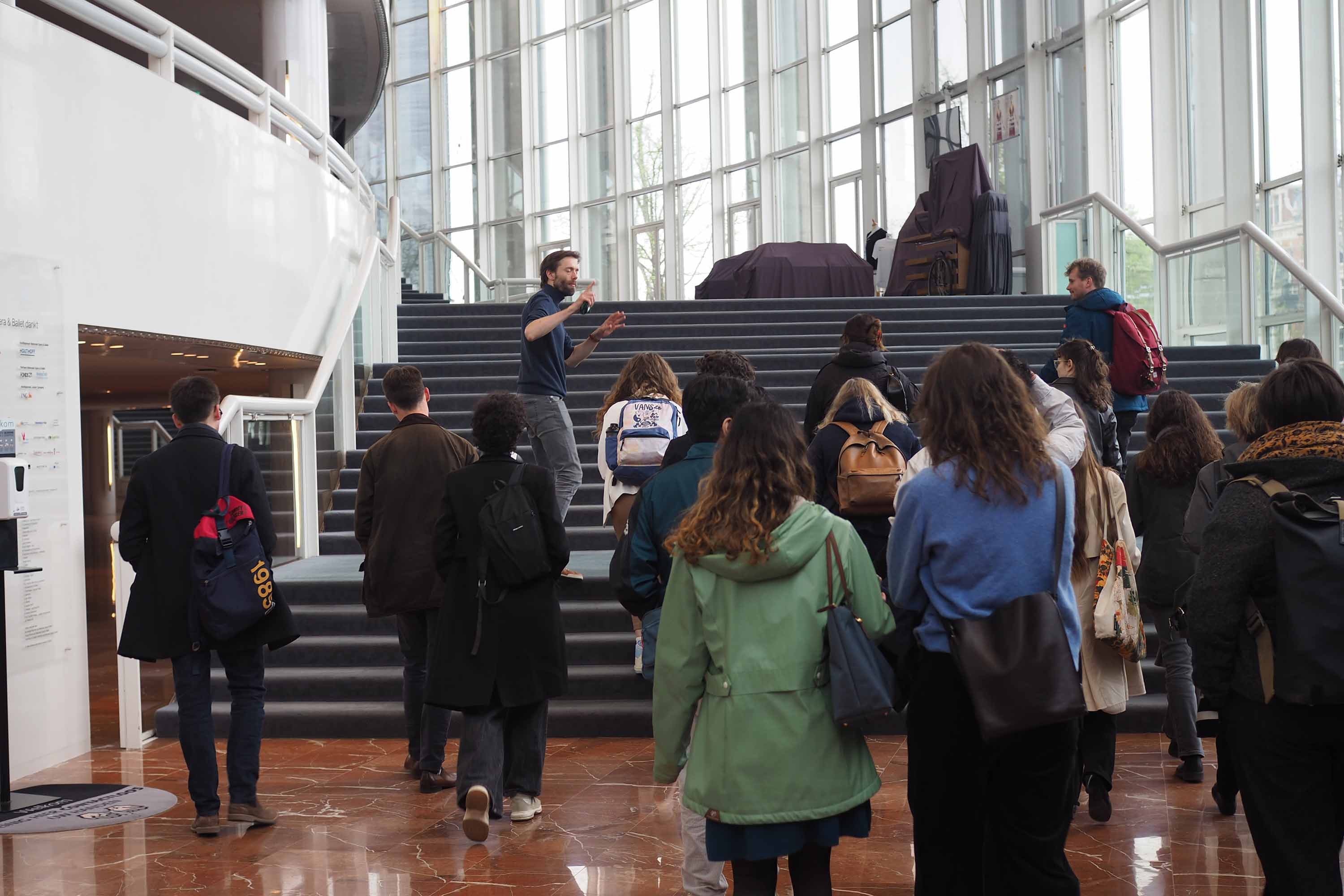 Medewerker van Nationale Opera loopt met studenten de trappen van het operahuis op.