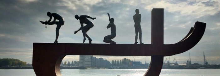 Foto van het slavernijmonument in Rotterdam. Op een gestileerd dansen vier figuren: de eerste tot slaafgemaakt is geketend en bij de vierde is de keten losgebroken.