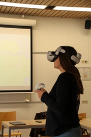 Een jonge vrouw met donkere kleding en donker haar draagt een witte VR-bril