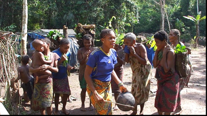 Joy from the forest group excursions being brought and spread back in the camp, while carrying their collected food and firewood. The full fledged singing event is also accompanied by energetic drumming and percussion with pans and cups