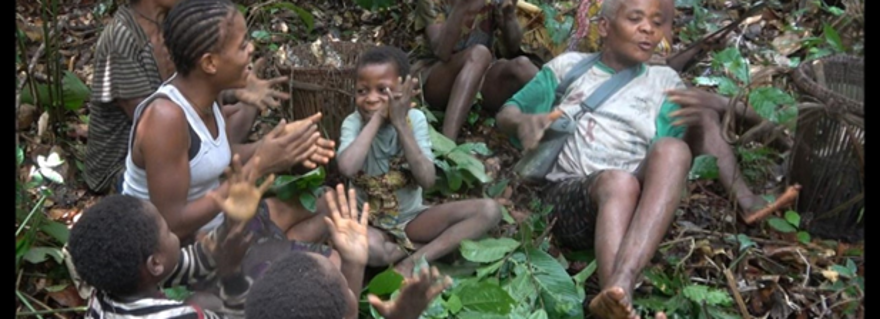A BaYaka group of women and girls singing and clapping enthusiastically while resting during a hectic day’s work in the forest