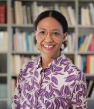 Een dame kijkt glimlachend in de lens. Op de achtergrond een boekenkast.